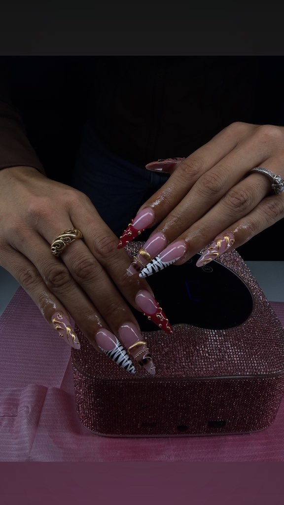 Client hands with gold-accented nails under a pink gel lamp